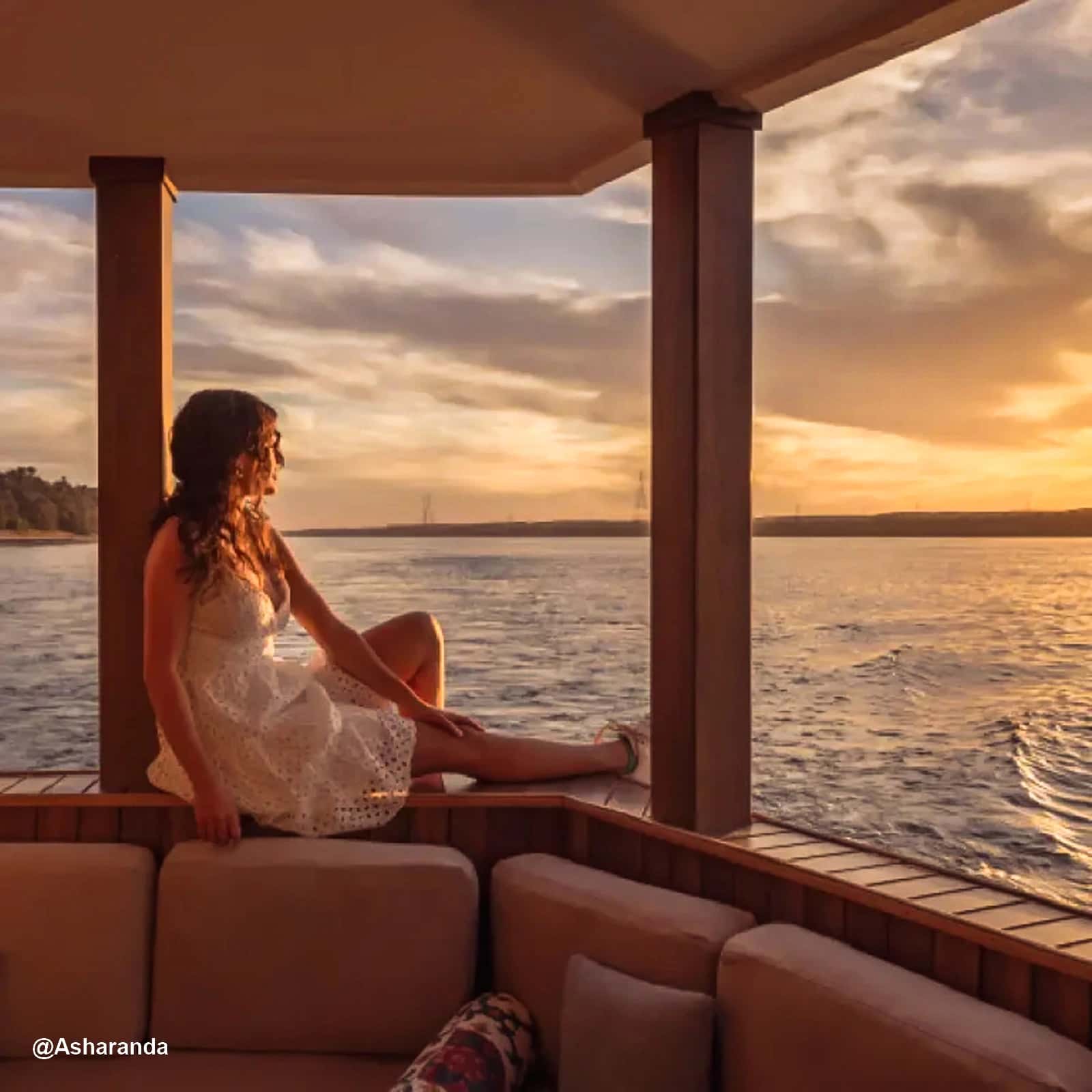 Contemplando el Atardecer desde una dahabeya en el Nilo Mujer con vestido blanco sentada en la esquina de un sofá al aire libre en una dahaeya en el Nilo, mirando el atardecer sobre el agua.