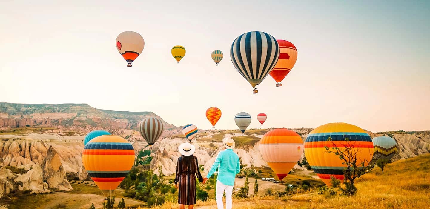 Capadocia en vuelo lento: un amanecer compartido sobre Anatolia Pareja contemplando globos aerostáticos al amanecer en Capadocia, una experiencia cultural y sensorial de viaje en Turquía